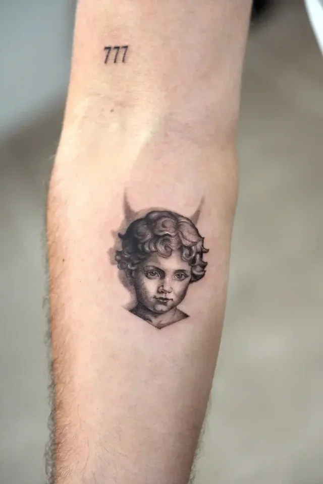 Illustratives Tattoo: fein schattierter Kinderkopf mit kleinen Hörnern auf dem Unterarm
