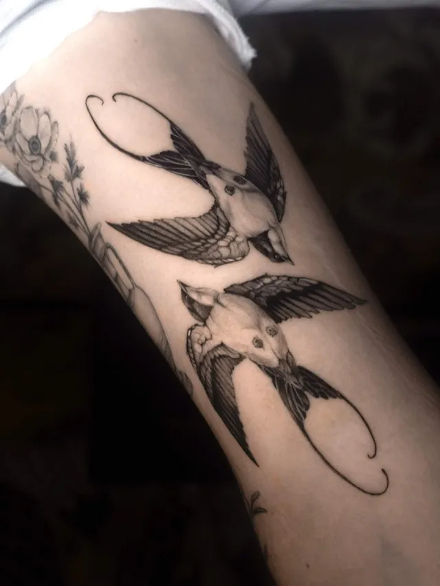 Traditional Tattoo: zwei Schwalben in kräftigem Schwarz-Grau auf dem Oberarm