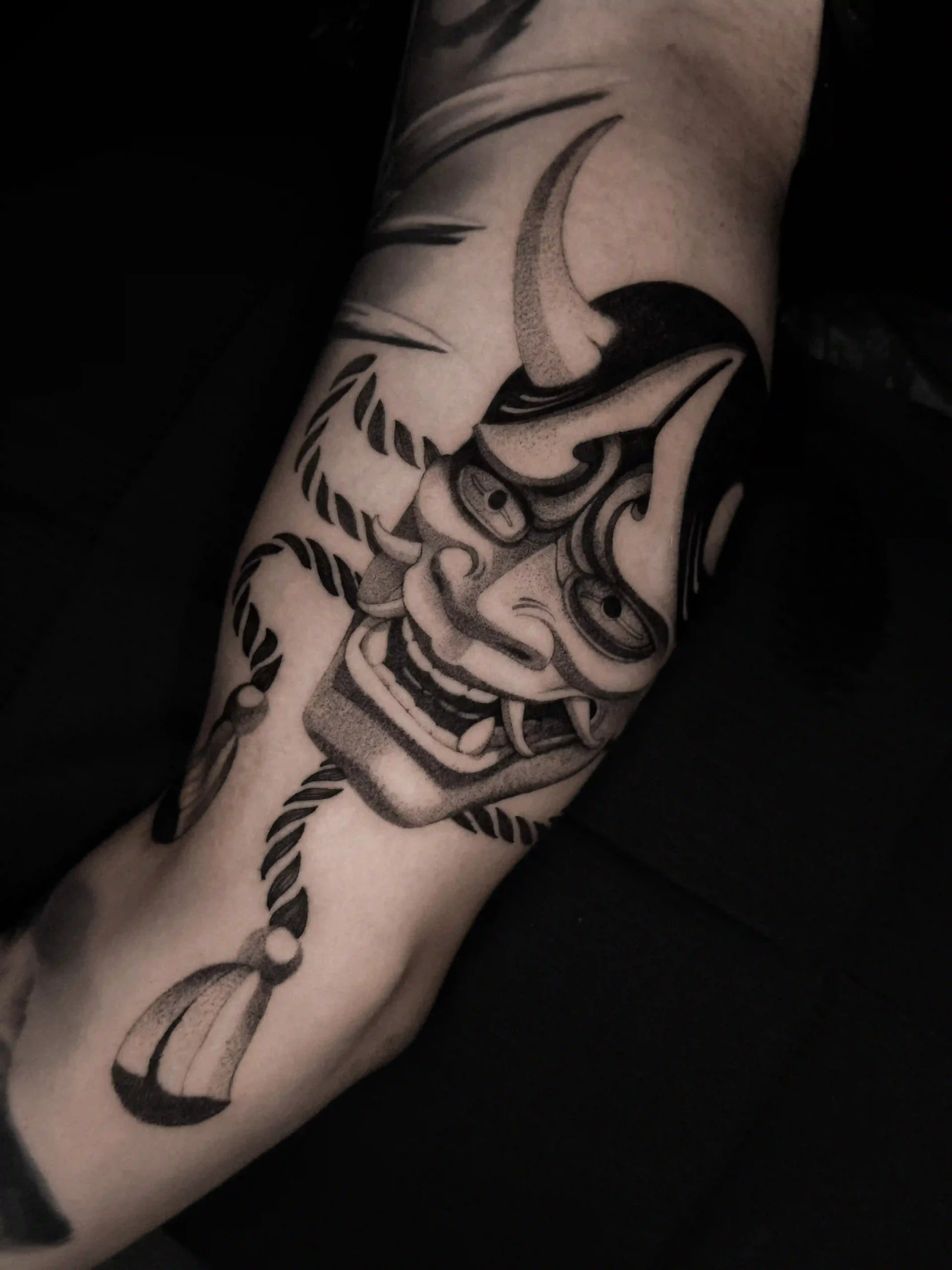Japanese hannya mask tattoo with bold black shading and rope details, featuring intense expression and traditional dotwork texture on the upper arm.