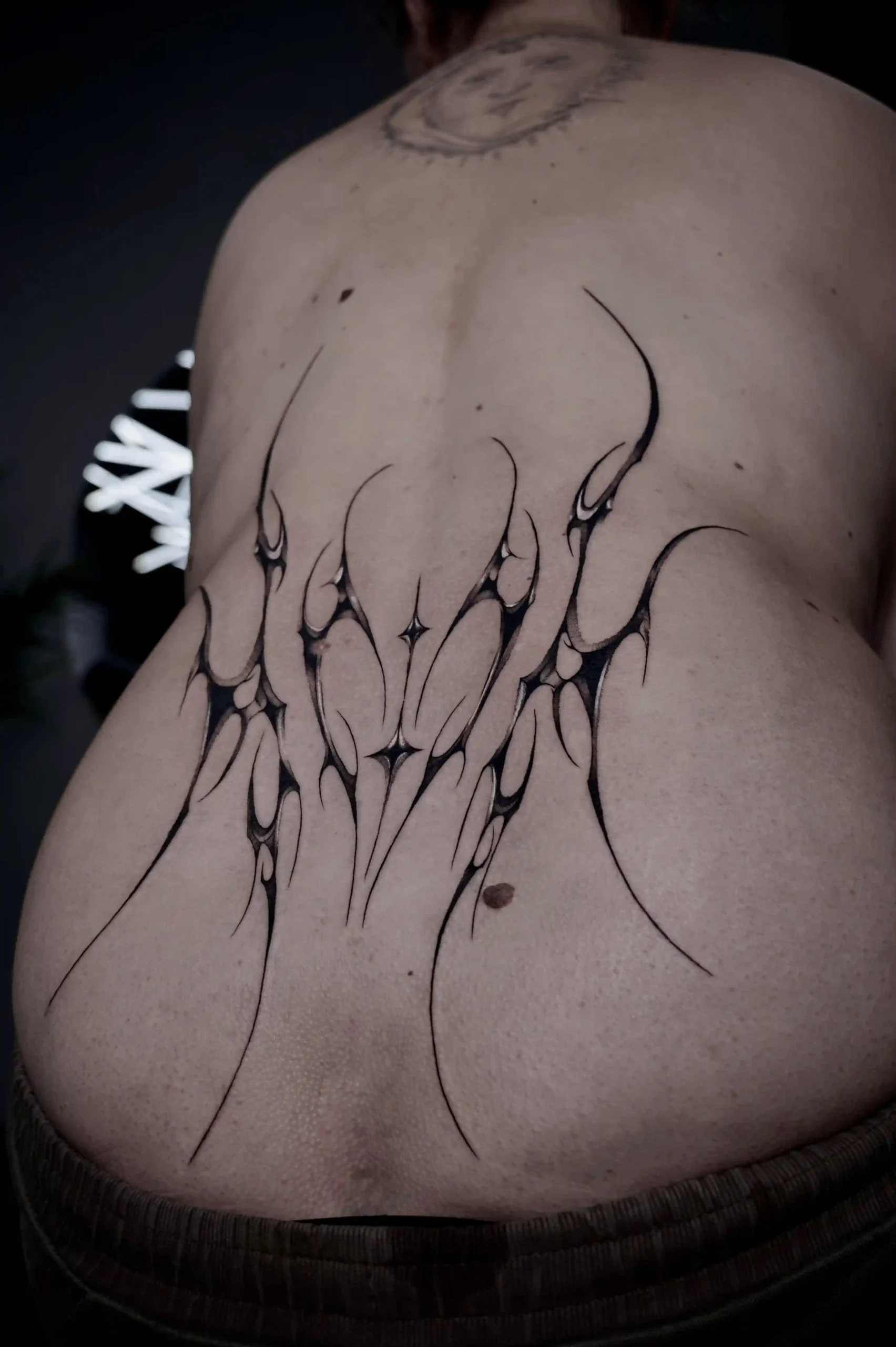 Abstract cyber sigilism tattoo on the lower back, composed of sharp symmetrical flame-like shapes with smooth gradients and negative space highlights.