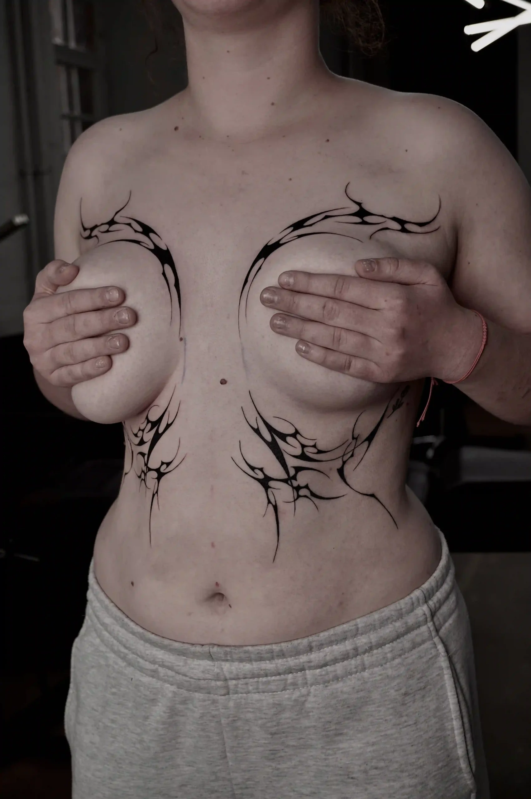 Abstract cyber sigilism tattoo design around the chest and under the breasts, composed of mirrored, flame-like shapes with bold contrast and clean negative space.